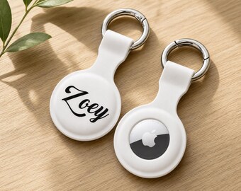 May include: Two white silicone protective cases for tracking devices, each featuring a silver metal keyring. One case displays the name Zoey in black script, while the other case holds a circular tracking device with a visible Apple logo.