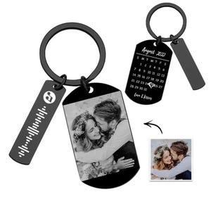 May include: Black metal keychains with personalized tags. One tag features a photo of a couple, another displays a calendar for August 2022 with a heart on the 24th, and the third has a music waveform. The words "Love & Kisses" are also on the calendar tag.