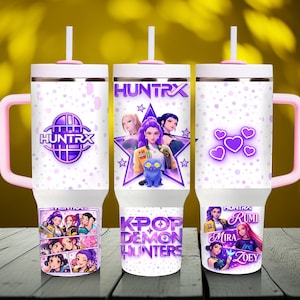 Può includere: Tre bicchieri isolanti bianchi con manici e coperchi rosa. Ogni bicchiere presenta un design diverso con il testo "HUNTRX" e grafica anime K-Pop. Uno ha un logo viola, un altro un design a stella e il terzo cuori viola.