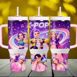 May include: Three K-Pop themed tumblers with pink handles, white lids, and straws. The tumblers feature illustrations of K-Pop singers and the text "K-POP" against a purple starry background with a rainbow. The tumblers are on a wooden surface.