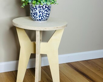 May include: A small, light-colored wooden plant stand with a round top and three legs. A blue and white patterned ceramic pot filled with green foliage sits on top. The stand is approximately 18 inches tall.