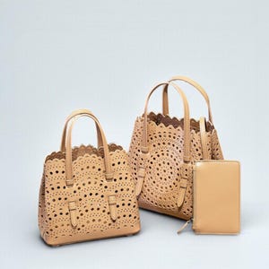 May include: Three beige leather handbags and a matching wallet. The handbags have a scalloped edge and a laser-cut design. The wallet has a zipper closure. The bags have top handles and adjustable shoulder straps.