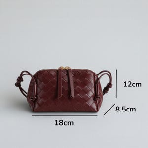 Pu&ograve; includere: Borsa a mano in pelle intrecciata bordeaux con cerniera superiore e manici annodati. La borsa misura 18 cm di lunghezza, 12 cm di altezza e 8,5 cm di larghezza. Ha una cerniera dorata e un tirazip in pelle abbinato.