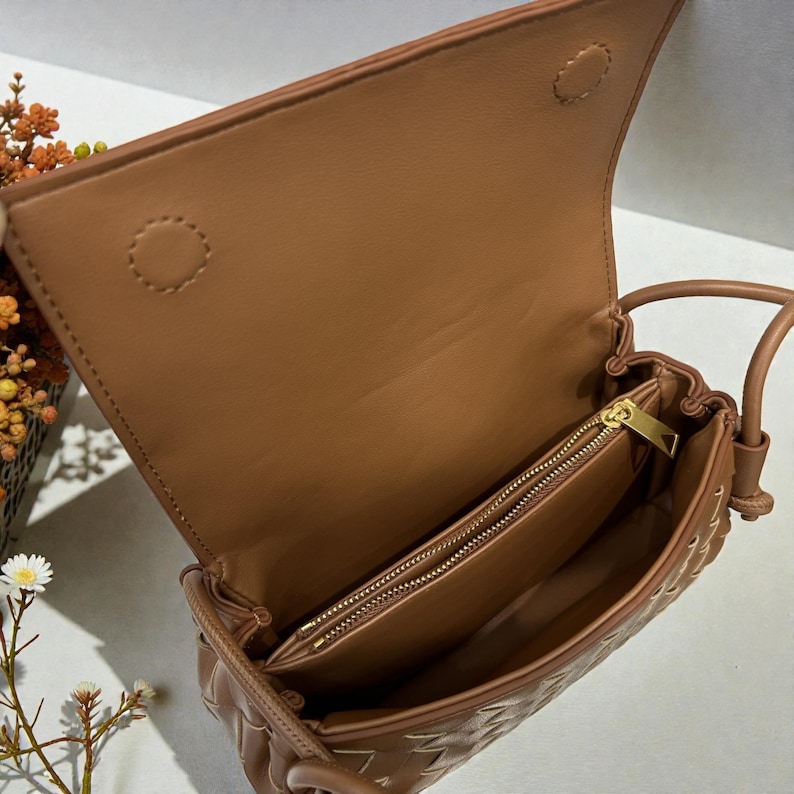 Puede incluir: Bolso de mano de cuero marr&oacute;n claro con un dise&ntilde;o tejido, abierto para mostrar el interior. El bolso tiene un cierre de solapa y un bolsillo interior con cremallera. El bolso es de color marr&oacute;n claro y tiene una correa para el hombro.