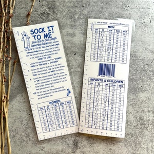 以下が含まれることがあります： 2つの白い「Sock It To Me」靴サイズ換算ガイド。男性用と女性・子供用があります。インチとセンチメートルでの測定値と、対応するヨーロッパとメキシコの靴のサイズが記載されています。テキストには説明が含まれています。