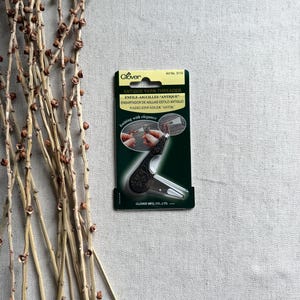 May include: A Clover Antique Yarn Threader on a neutral background. The package is dark green with white text and a picture of the threader in use. The threader is black with a decorative handle. The text "knitting with elegance" is also visible.