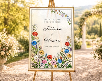 Puede incluir: Un letrero de boda rectangular de cristal en un marco dorado sobre un caballete. El letrero presenta texto negro que dice WELCOME TO OUR WEDDING, Jillian & Henry, y 10.20.2026, rodeado por un borde floral colorido con flores rojas, azules, amarillas y rosas.