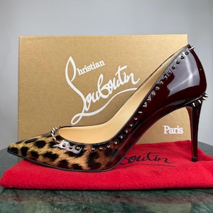 Peut inclure: Escarpins à talons hauts bordeaux avec bout léopard et détails cloutés argentés. Les talons aiguilles et la finition brillante sont mis en valeur. La marque "Christian Louboutin" est visible sur la boîte.