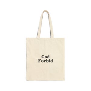 May include: A cream-colored tote bag with the words "God Forbid" printed in black, centered on the front. The bag has two matching handles for carrying.