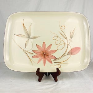 May include: A rectangular off-white ceramic serving platter featuring a central pink star-shaped flower illustration, accented by delicate brown line-drawn leaves, stems, and swirling tendrils that extend across the surface of the dish.