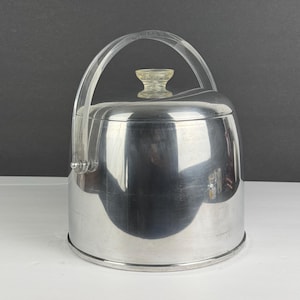 May include: A vintage, stainless steel ice bucket with a clear acrylic handle and lid knob. The bucket has a rounded shape and a reflective surface, with a clear handle that arches over the top. The lid features a decorative knob.