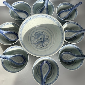 May include: A large central bowl and seven smaller bowls, each accompanied by a matching spoon. The white ceramic set features blue dragon motifs and intricate lattice patterns. The bowls have translucent rice grain designs along the rims.