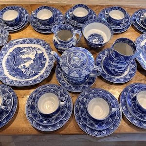 May include: A large collection of blue and white ceramic dinnerware featuring intricate landscape patterns. The set includes multiple teacups with matching saucers, a teapot, a creamer, a sugar bowl, several plates, and two serving bowls.