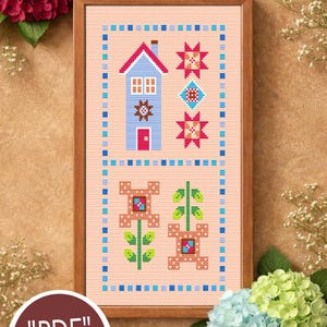 Puede incluir: Patrón de punto de cruz enmarcado con una casa azul, estrellas y elementos florales. El diseño incluye el texto "Candy Stitch" y "PDF PATTERN" sobre un fondo beige. El marco es de color marrón claro.