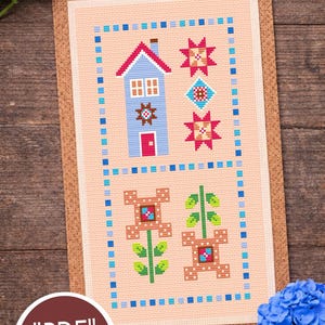 Puede incluir: Patrón de punto de cruz con una casa azul, estrellas y flores en un diseño enmarcado. El diseño está sobre un fondo color melocotón con un borde azul. También se ve el texto "PDF" y "Candy Stitch".