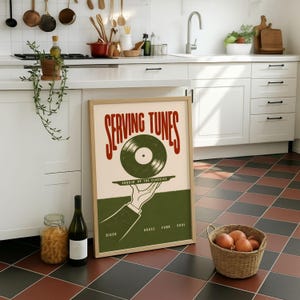 Peut inclure: Une affiche encadrée avec le texte "SERVING TUNES" en rouge, représentant un disque vinyle vert sur un plateau tenu par une main. L'affiche comprend également les mots "COOKIN' UP THE CLASSICS" et les genres musicaux "DISCO, HOUSE, FUNK, SOUL".