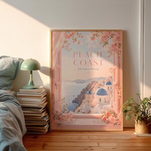 Könnte beinhalten: Ein gerahmter Kunstdruck mit dem Titel "Peach Coast" zeigt eine Küstenlandschaft mit weißen Gebäuden, blauen Kuppeln und rosa Blumen. Das Kunstwerk ist in einem rosa Fensterrahmen gesetzt und erzeugt eine ruhige, sonnendurchflutete Atmosphäre. Der Druck wird auf einem Holzboden präsentiert.