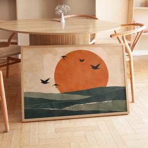 Può includere: Una stampa artistica rettangolare incorniciata con un grande sole arancione centrato su un cielo beige pallido. Sotto il sole, colline sovrapposte verde scuro sono raffigurate con bordi di carta strappata. Quattro sagome di uccelli neri volano.