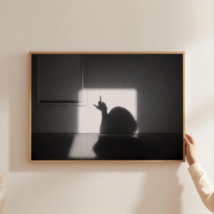 Könnte beinhalten: Schwarz-weiß gerahmter Kunstdruck. Das Bild zeigt eine Silhouette des Kopfes und der Hand einer Person, wobei der Mittelfinger erhoben ist. Das Kunstwerk ist vor einer hellen, quadratischen Lichtquelle platziert.