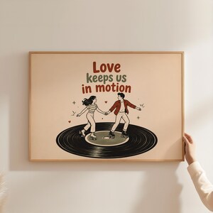 May include: A rectangular framed wall art print on a beige background featuring a black vinyl record with two people roller skating on it. The text reads Love keeps us in motion in red and green letters, accompanied by small red hearts and stars.