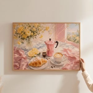 Könnte beinhalten: Ein gerahmter Wandkunstdruck, der eine Frühstücksszene auf einem Tisch zeigt, mit einer rosa Mokkakanne, einer Tasse Latte mit Milchschaum, einem Croissant auf einem Teller, Zitronenscheiben, einem Glas Espresso und einer Vase mit gelben Blumen.