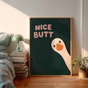 Könnte beinhalten: Ein rechteckiger Wandkunstdruck mit dunkelgrünem Hintergrund, dem Text NICE BUTT in hellrosa Buchstaben und einer Cartoon-Illustration einer weißen Gans mit orangefarbenem Schnabel, die aus der unteren rechten Ecke ins Bild schaut.