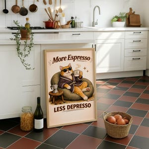 Könnte beinhalten: Ein gerahmtes Poster mit dem Text "More Espresso Less Depresso" zeigt eine Cartoon-Katze mit Sonnenbrille und Bademantel, die eine Kaffeetasse hält. Die Katze sitzt in einem Sitzsack. Eine kleine Espressomaschine steht auf einem Hocker.