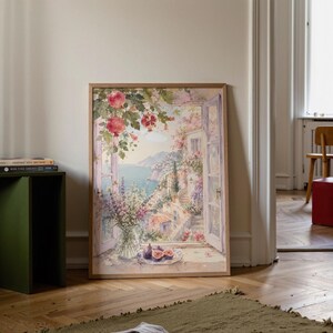 Könnte beinhalten: Ein gerahmtes Aquarellbild, das ein offenes Fenster mit Blick auf eine Küstenstadt zeigt. Die Szene umfasst eine Glasvase mit Blumen, einen Teller mit Feigen und Granatapfelzweige, die in Rosa- und Grüntönen über den Fensterrahmen hängen.