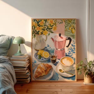 Könnte beinhalten: Ein gerahmter Kunstdruck, der ein Stillleben mit einer rosa Mokkakanne, einer Tasse Kaffee mit Latte Art, einem Croissant auf einem Teller, einer kleinen Schale mit Zitronenscheiben und einem weißen Krug mit gelben Blumen zeigt.