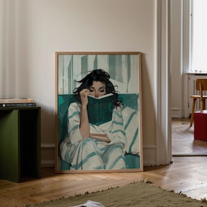 Könnte beinhalten: Ein gerahmter Kunstdruck zeigt eine Frau, die in ein Buch vertieft ist. Sie trägt einen weiß-blau gestreiften Bademantel und sitzt auf einer türkisfarbenen Oberfläche. Das Kunstwerk hat eine Vintage-Ästhetik mit Holzrahmen und neutralem Hintergrund.