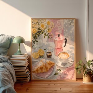 Könnte beinhalten: Ein gerahmter Kunstdruck, der eine Frühstücksszene mit einer Glasvase voller gelber Blumen, einer rosa Mokkakanne, einer Tasse Latte mit herzförmigem Milchschaum, einem Glas Espresso, zwei Zitronenscheiben und einem Croissant zeigt.