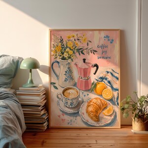 Könnte beinhalten: Ein gerahmter Kunstdruck mit einem Stillleben aus einer weißen Kanne mit gelben Blumen, einer rosa Espressokanne, einer Tasse Kaffee, einem Croissant und Orangenscheiben. Der Text coffee joy sunshine ist in blauer Schrift auf dem Bild zu sehen.