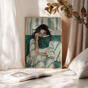 Könnte beinhalten: Ein gerahmter Kunstdruck zeigt eine Person, die ein Buch liest. Das Kunstwerk zeigt eine Person in einem gestreiften Gewand, die auf einem türkisfarbenen Sofa sitzt. Das Buch ist grün, und der Hintergrund hat vertikale Streifen. Der Rahmen ist hellholzfarben.