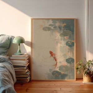 Puede incluir: Una impresión artística enmarcada que representa un pez koi nadando en un estanque con nenúfares. La obra de arte tiene una paleta de colores suaves de beige, verde azulado y naranja. El marco de madera añade un toque natural a la escena serena.