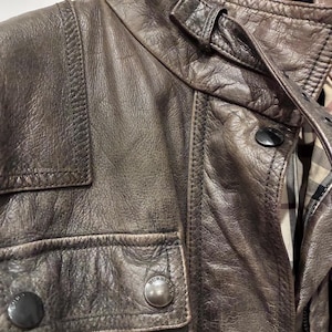 Primo piano giacca Burberry in pelle marrone multitasche, chiusura con zip e bottoni. Cintura in vita.