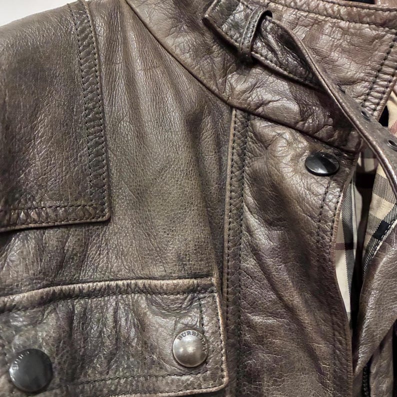 Primo piano giacca Burberry in pelle marrone multitasche, chiusura con zip e bottoni. Cintura in vita.