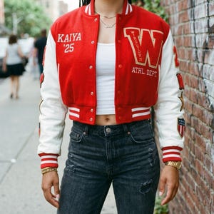 May include: A red and white varsity jacket featuring the text KAIYA '25 on the right chest and a large letter W with the text WIRGETDNN ATHL. DEPT. on the left chest. The sleeves are white with red striped cuffs and various patches including a star and shield.