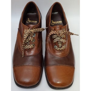 May include: A pair of two-tone brown leather shoes with striped laces. The shoes have a rounded toe and the brand name "Jarman SHOES FOR MEN" is visible on the inner sole.