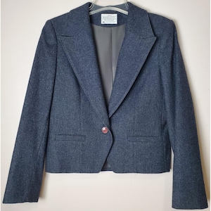 May include: A dark blue blazer with a single red button closure. The blazer has a classic notched lapel and two front pockets. The interior lining is a dark gray color. The blazer is hanging on a hanger.