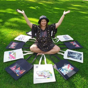 Puede incluir: Una colección de bolsas de mano con varios diseños arquitectónicos coloridos. Las bolsas son negras y blancas, con imágenes de edificios y arte. Las bolsas están dispuestas sobre un césped verde.