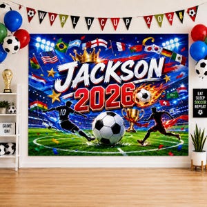 May include: A soccer-themed party backdrop featuring the name JACKSON and the year 2026 in large, bold text. The design includes two soccer players, a soccer ball, a gold trophy, and various international flags against a stadium background.