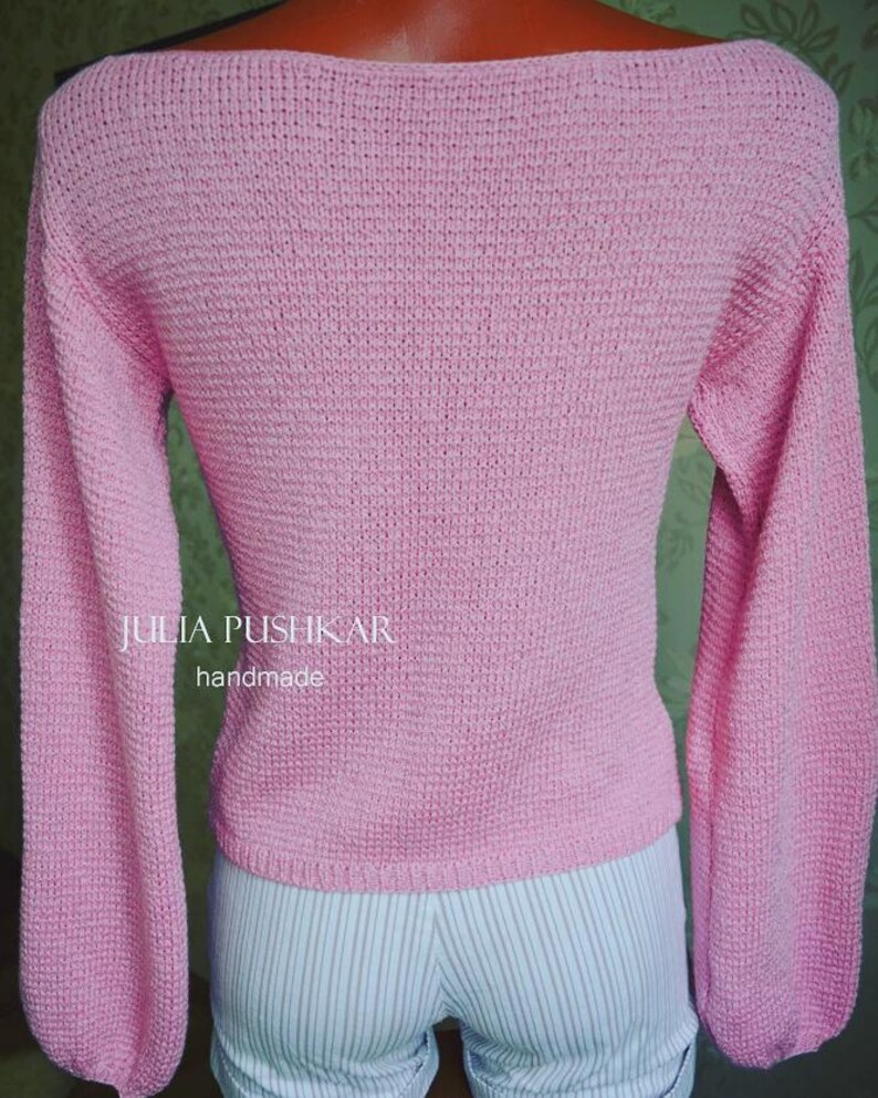 May include: A light pink, handmade knitted jumper with long sleeves and a boat neck. The jumper has a textured knit pattern and the text "JULIA PUSHKAR handmade" is visible on the front.