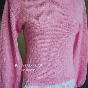 May include: A pale pink knitted jumper with long, balloon sleeves and a wide boat neck. The sleeves are gathered at the wrist. The text "JULIA PUSHKAR handmade" is visible on the front.