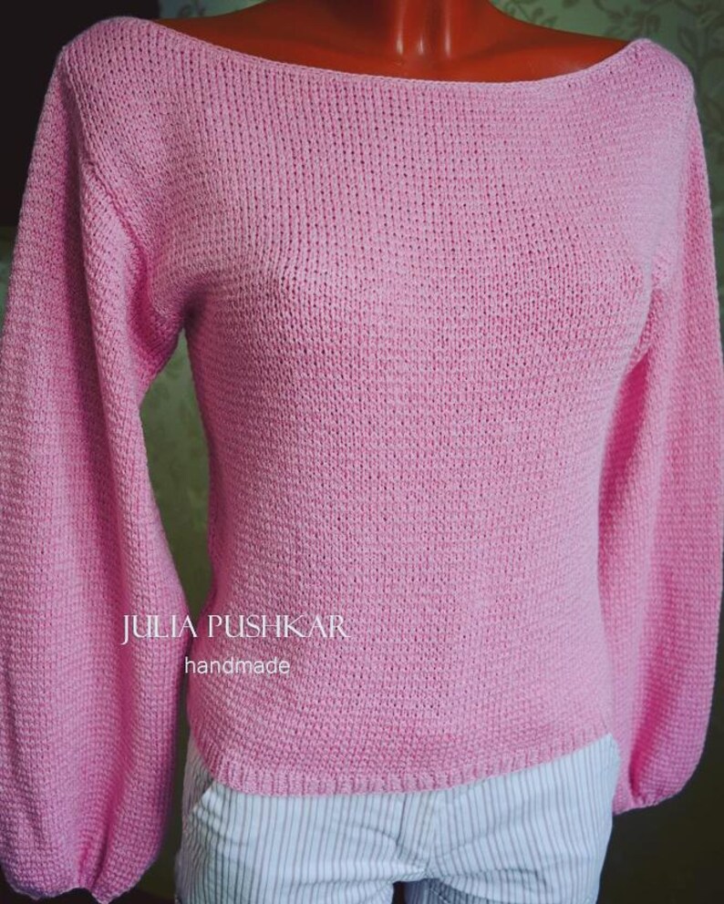 May include: A pale pink knitted jumper with long, balloon sleeves and a wide boat neck. The sleeves are gathered at the wrist. The text "JULIA PUSHKAR handmade" is visible on the front.