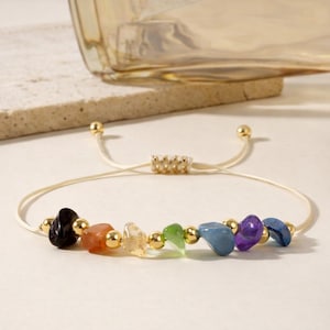 Op de afbeelding: Verstelbare armband met zeven gekleurde edelstenen die de chakra's vertegenwoordigen. De stenen zijn zwart, oranje, helder, groen, blauw, paars en donkerblauw. Er zijn ook goudkleurige kralen en accenten.