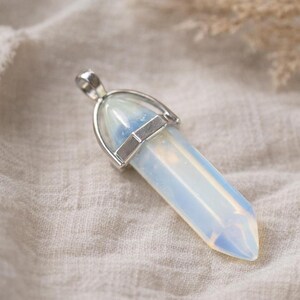 Pode incluir: Um pingente de cristal opalino polido com uma tampa de metal prateado. O cristal é de cor azul pálido e branco, com uma extremidade pontiaguda. O pingente foi projetado para ser usado como joia.