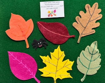 May include: A green felt board featuring a black spider and five colorful felt leaves in orange, maroon, pink, yellow, and light green. A white card with the text "Little spider, little spider Playing hide and seek Are you under the ____ leaf? Let's take a peek!" is included. The base is labeled "Friendly Faces Felt."