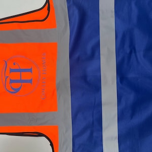 May include: An orange safety vest with reflective stripes and a blue logo that reads "Colley Homes". The vest also has a blue section with reflective stripes.