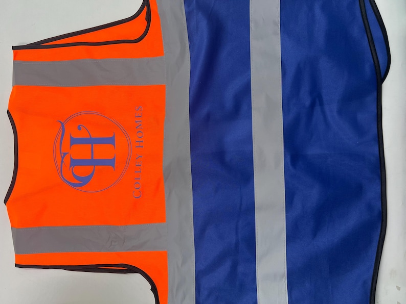 May include: An orange safety vest with reflective stripes and a blue logo that reads "Colley Homes". The vest also has a blue section with reflective stripes.