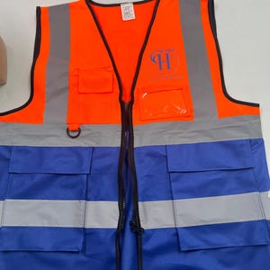 May include: High-visibility safety vest in bright orange and blue. The vest features reflective silver stripes and a black zipper. It has multiple pockets and a logo on the chest. The vest is designed for enhanced visibility.